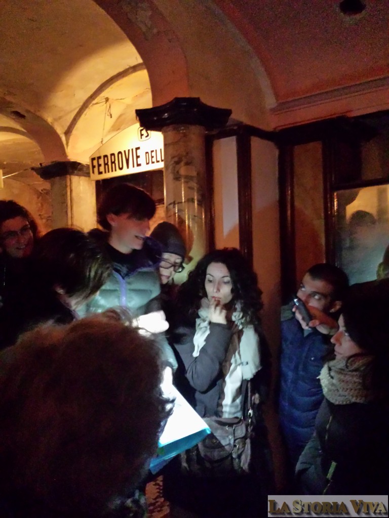 La guida volontaria del FAI Laura Bronzini illustra la storia del Diurno al gruppo di visitatori. Notare alle spalle l'insegna della biglietteria ferroviaria.